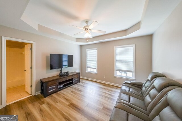 living room with light wood-type flooring, a raised ceiling, and ceiling fan