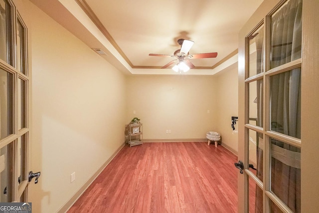 empty room featuring french doors, ceiling fan, ornamental molding, a tray ceiling, and wood-type flooring