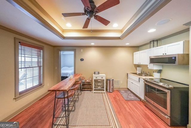 kitchen featuring white cabinetry, stainless steel appliances, a raised ceiling, light hardwood / wood-style flooring, and crown molding