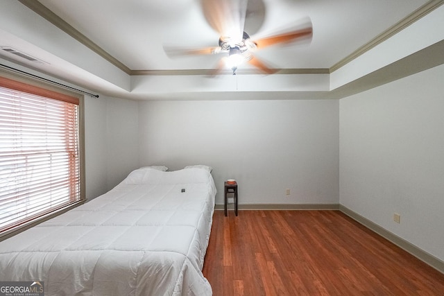 bedroom featuring dark wood-type flooring, a tray ceiling, ceiling fan, and ornamental molding