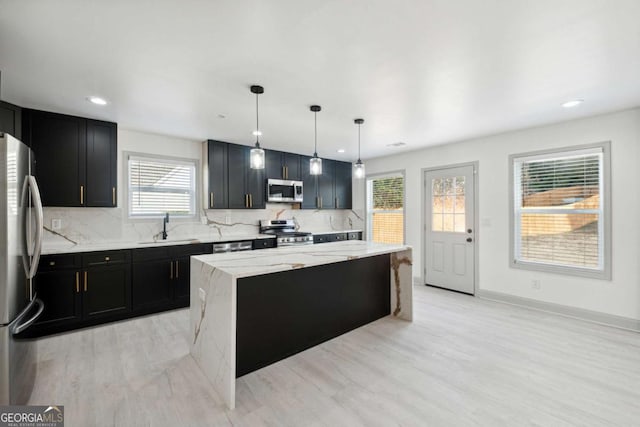 kitchen with appliances with stainless steel finishes, decorative light fixtures, a kitchen island, and a healthy amount of sunlight