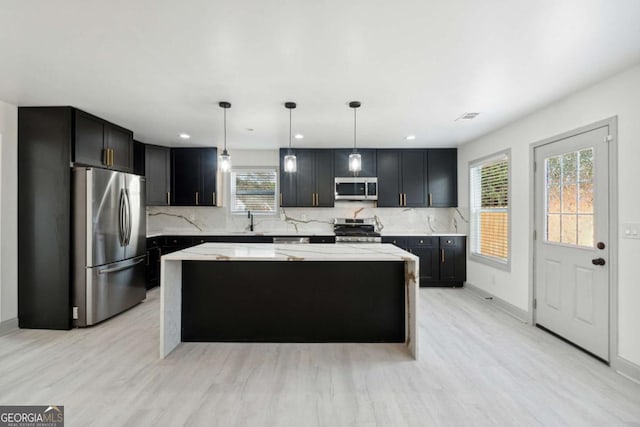 kitchen with light stone counters, stainless steel appliances, decorative light fixtures, a center island, and light hardwood / wood-style floors