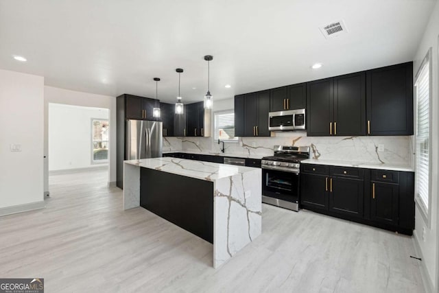 kitchen with pendant lighting, plenty of natural light, a kitchen island, and appliances with stainless steel finishes