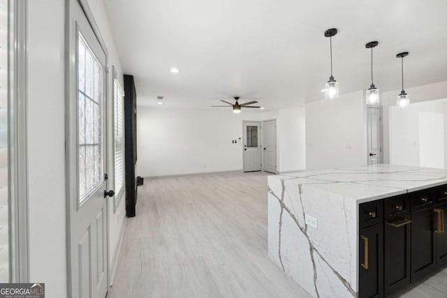 kitchen with ceiling fan, light stone counters, hanging light fixtures, and light hardwood / wood-style flooring