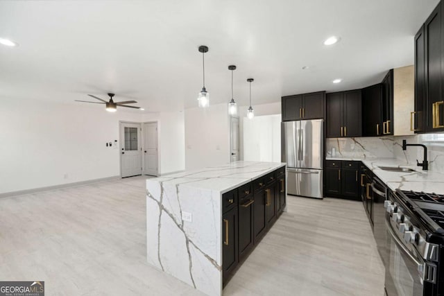 kitchen featuring ceiling fan, sink, a center island, light stone counters, and appliances with stainless steel finishes