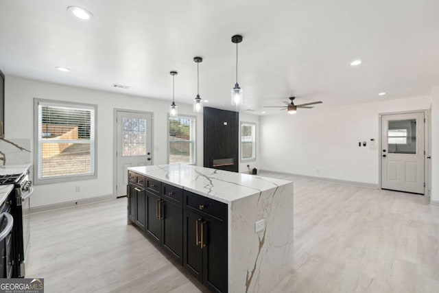 kitchen featuring ceiling fan, a center island, hanging light fixtures, light stone counters, and light wood-type flooring