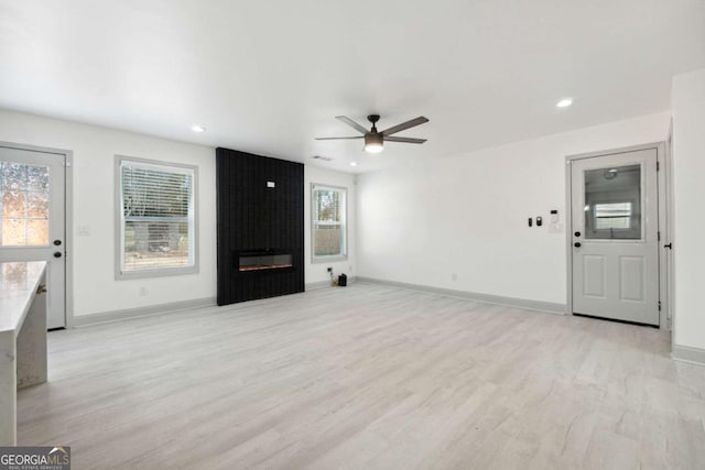 unfurnished living room featuring ceiling fan, a large fireplace, and light wood-type flooring