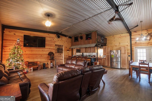 living room with a chandelier, wooden walls, wood-type flooring, and vaulted ceiling