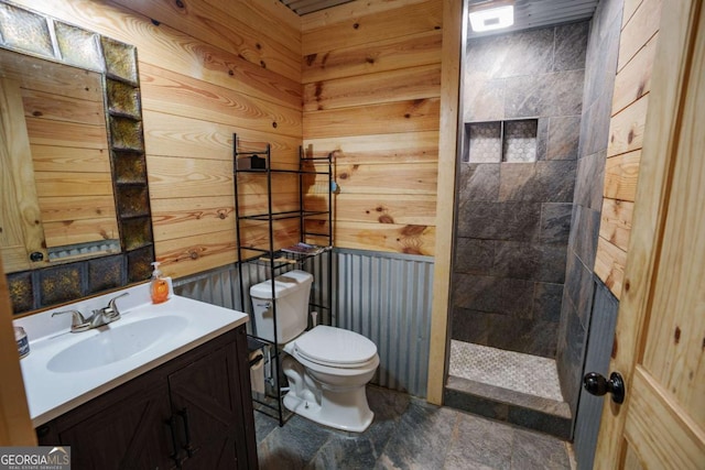 bathroom with vanity, wood walls, toilet, and tiled shower