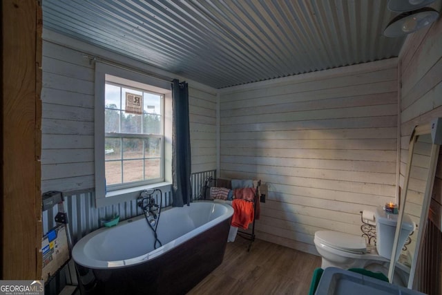 bathroom with a bathing tub, wood walls, toilet, and hardwood / wood-style flooring