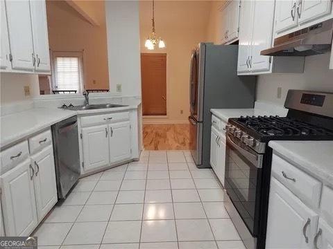 kitchen featuring stainless steel appliances, sink, light tile patterned floors, decorative light fixtures, and white cabinets