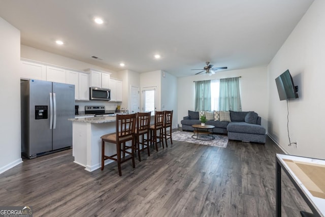 kitchen with stainless steel appliances, a center island, dark hardwood / wood-style floors, white cabinetry, and a breakfast bar area