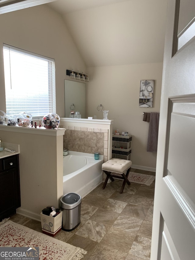 bathroom featuring vanity, a bath, and vaulted ceiling