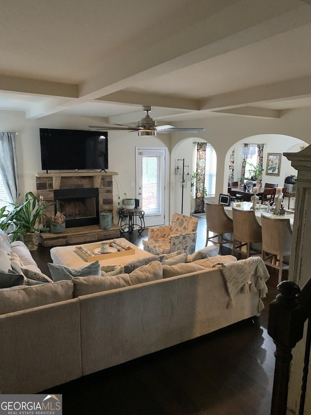 living room featuring beam ceiling, ceiling fan, a fireplace, and wood-type flooring