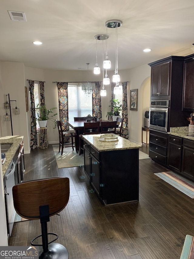 kitchen with appliances with stainless steel finishes, light stone counters, dark wood-type flooring, decorative light fixtures, and a kitchen island