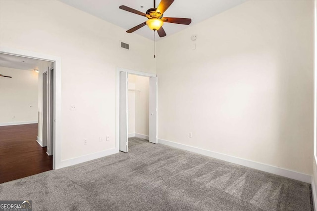 unfurnished bedroom with a high ceiling, dark carpet, and ceiling fan