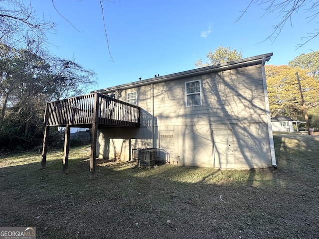 back of property with a deck, cooling unit, and a lawn