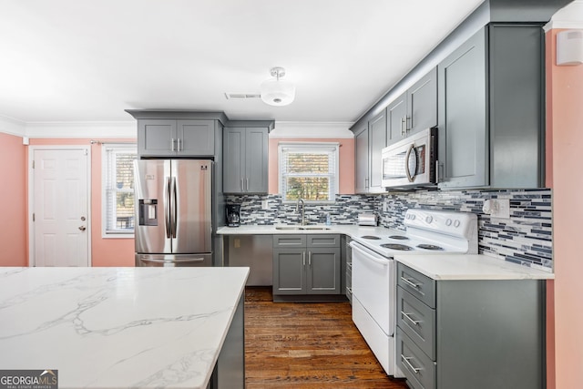 kitchen with light stone countertops, ornamental molding, stainless steel appliances, sink, and gray cabinets