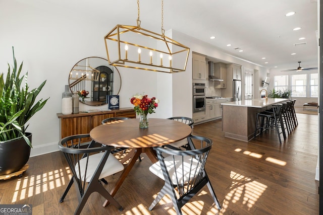 dining space with sink, dark wood-type flooring, and ceiling fan with notable chandelier