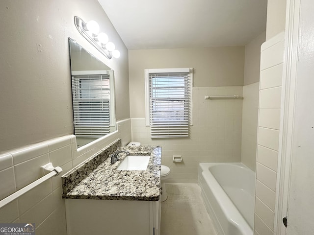 bathroom featuring vanity, a tub to relax in, toilet, and tile walls