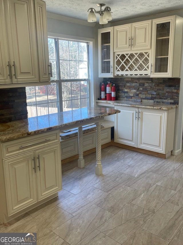 kitchen with light stone counters, a notable chandelier, backsplash, cream cabinets, and a textured ceiling