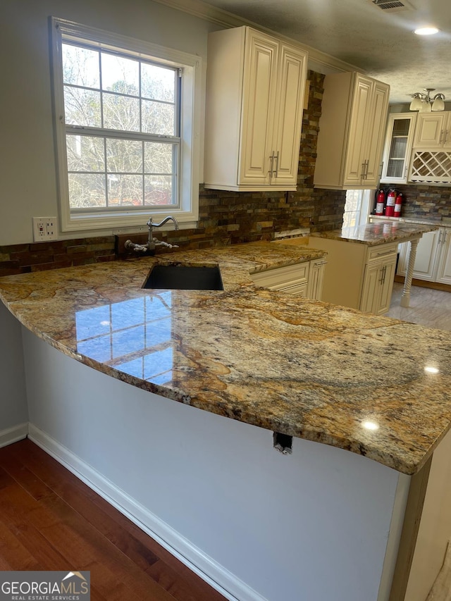 kitchen with hardwood / wood-style flooring, stone countertops, kitchen peninsula, and sink