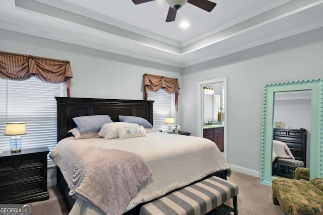 bedroom featuring a raised ceiling, ceiling fan, ornamental molding, connected bathroom, and light colored carpet