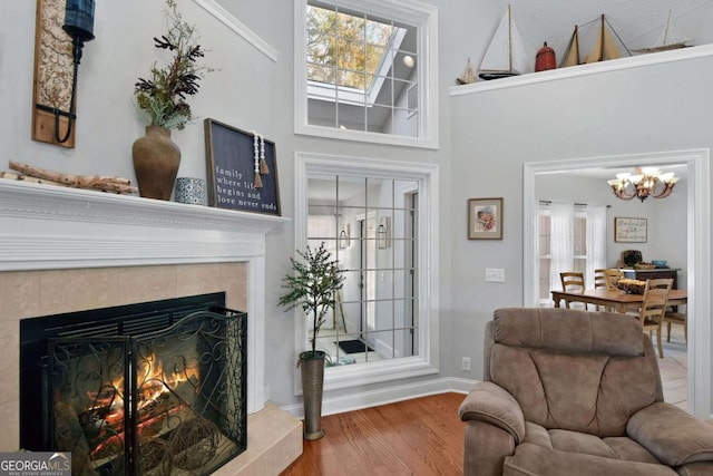 living room with a fireplace, wood-type flooring, a towering ceiling, and an inviting chandelier