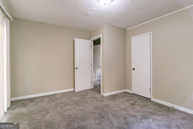 unfurnished bedroom featuring light carpet, a textured ceiling, a closet, and ornamental molding