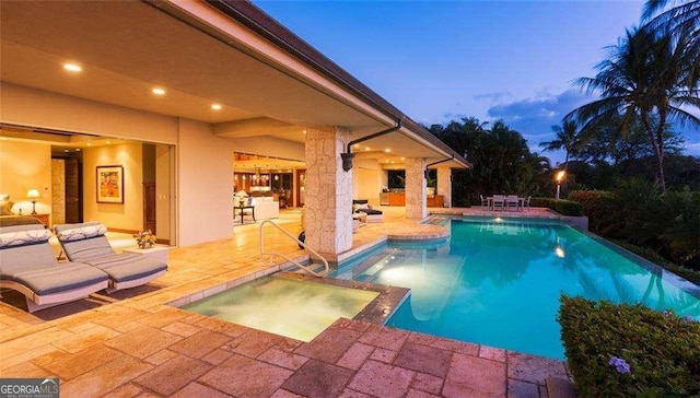 pool at dusk with an in ground hot tub and a patio