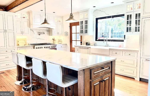 kitchen featuring light hardwood / wood-style floors, pendant lighting, a center island, stainless steel stove, and white cabinetry