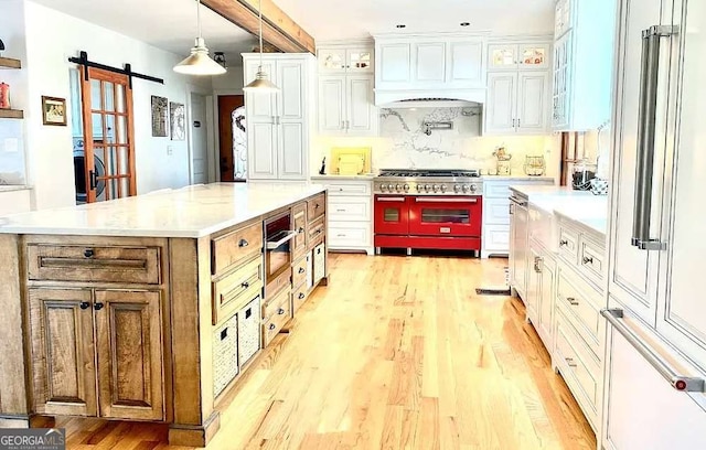 kitchen featuring light wood-type flooring, a barn door, double oven range, a center island, and white cabinetry