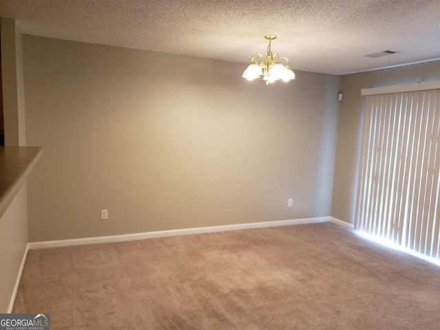 carpeted spare room featuring a textured ceiling and an inviting chandelier