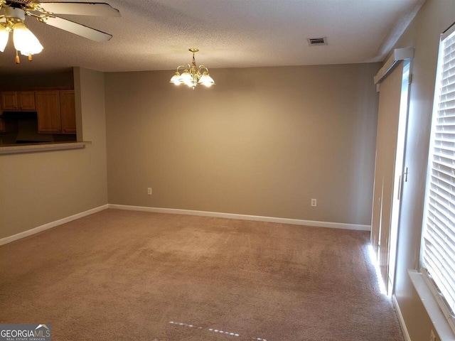 carpeted spare room with ceiling fan with notable chandelier and a textured ceiling