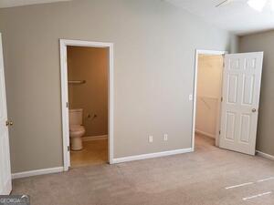 unfurnished bedroom featuring connected bathroom, a walk in closet, light carpet, and a closet