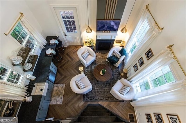 living room with a fireplace, dark parquet floors, a towering ceiling, and plenty of natural light