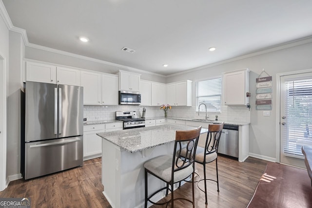 kitchen featuring light stone countertops, appliances with stainless steel finishes, sink, white cabinets, and a kitchen island