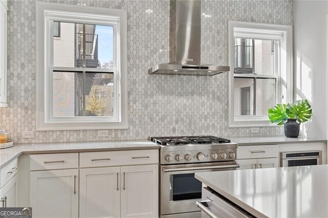 kitchen with a healthy amount of sunlight, white cabinetry, stainless steel appliances, and wall chimney range hood