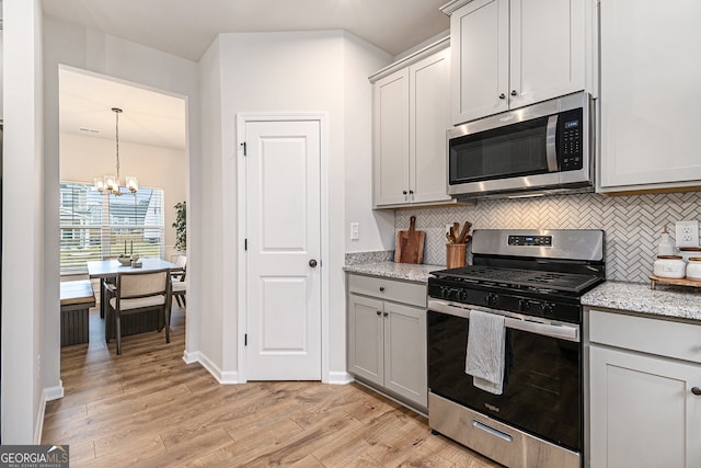 kitchen featuring tasteful backsplash, light wood-type flooring, stainless steel appliances, and an inviting chandelier