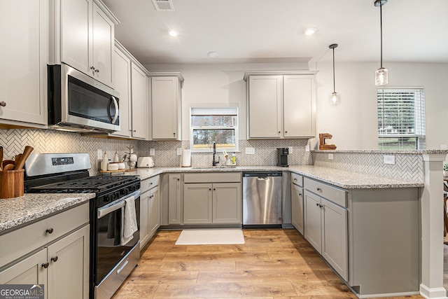 kitchen with sink, stainless steel appliances, light hardwood / wood-style flooring, pendant lighting, and decorative backsplash