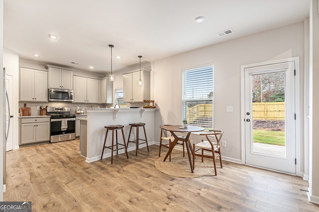 kitchen featuring hanging light fixtures, appliances with stainless steel finishes, light hardwood / wood-style floors, kitchen peninsula, and a breakfast bar area