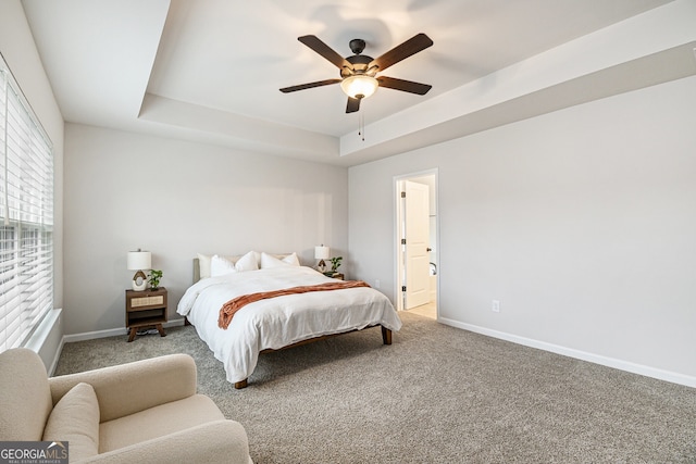 carpeted bedroom featuring ceiling fan, ensuite bathroom, and a tray ceiling