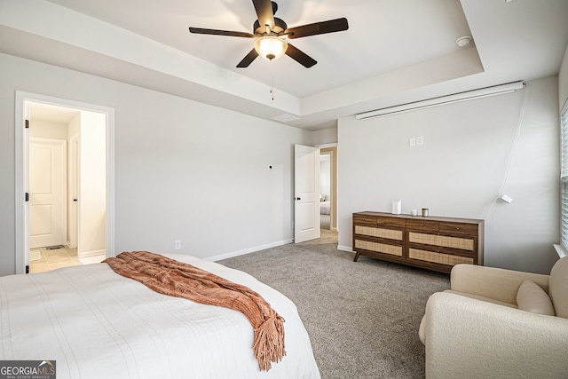 bedroom with carpet flooring, a tray ceiling, ceiling fan, and ensuite bathroom