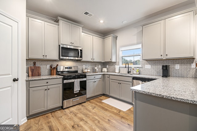 kitchen featuring sink, light hardwood / wood-style flooring, light stone countertops, appliances with stainless steel finishes, and tasteful backsplash