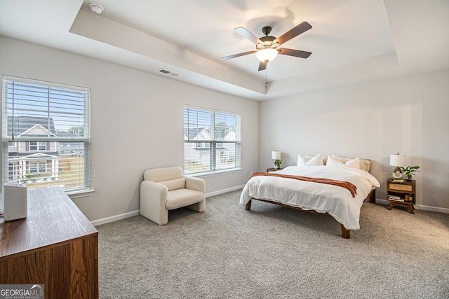 carpeted bedroom with a raised ceiling and ceiling fan