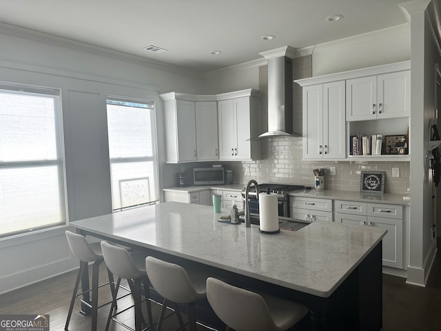 kitchen with white cabinets, an island with sink, and wall chimney range hood