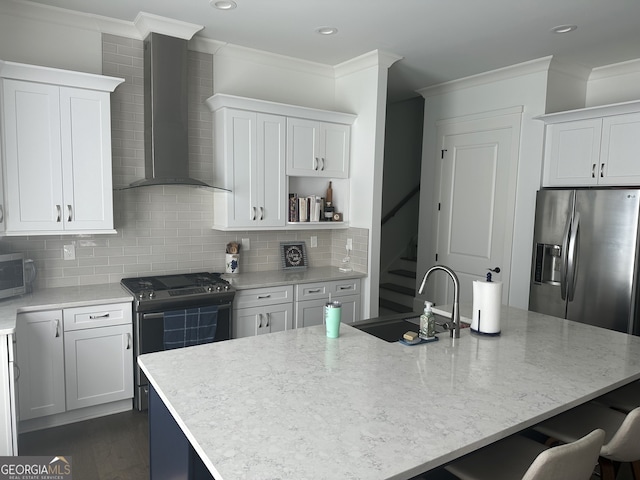 kitchen featuring white cabinetry, wall chimney range hood, a center island with sink, appliances with stainless steel finishes, and ornamental molding