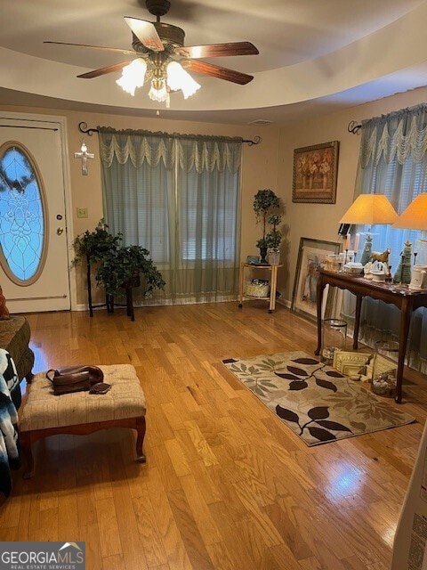 sitting room featuring a raised ceiling, ceiling fan, and wood finished floors