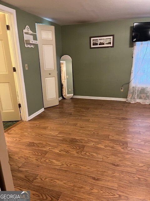 empty room with arched walkways, baseboards, and wood finished floors