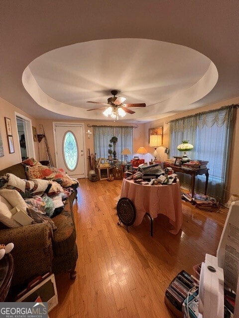 living area featuring a raised ceiling, wood finished floors, and a ceiling fan